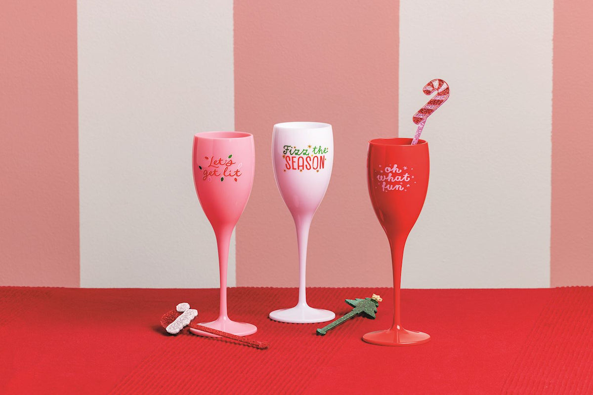 Let's Get Lit Acrylic Champagne Flute and Stirrer Set, A pink acrylic champagne flute lettered Let's get lit in red, wrapped in a cello sleeve with red and green confetti and a stirrer, tied with a red ribbon.
