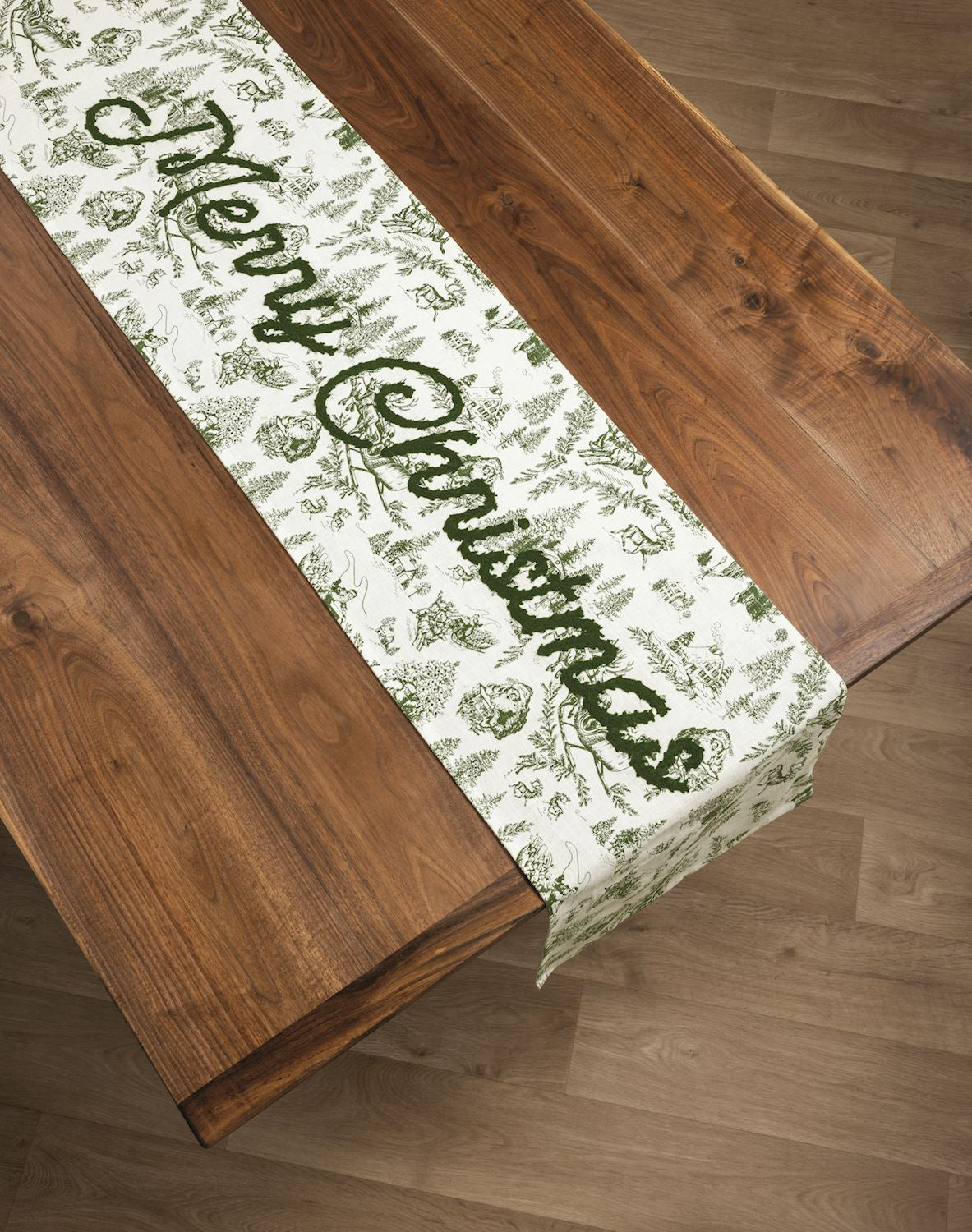 Green Toile Merry Christmas Table Runner, A long cream cotton table runner printed in green Christmas toile with Merry Christmas embroidered in green script across the center.