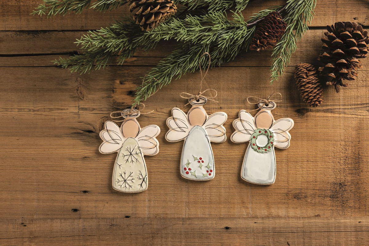 Snowflake Angel Stoneware Ornament, 5.25 Inch, A flat speckled cream stoneware angel ornament with sketched black line wings, a halo and snowflakes on the gown, hanging from a twine loop tied in a small bow.