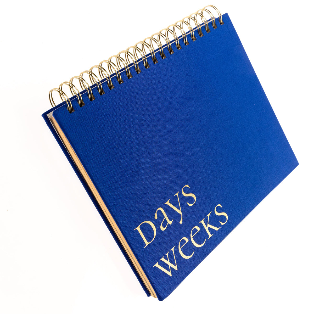 Cobalt Blue Fabric-Bound Weekly Desk Pad, A cobalt blue fabric desk pad reading days weeks in gold foil with a spiral top binding.
