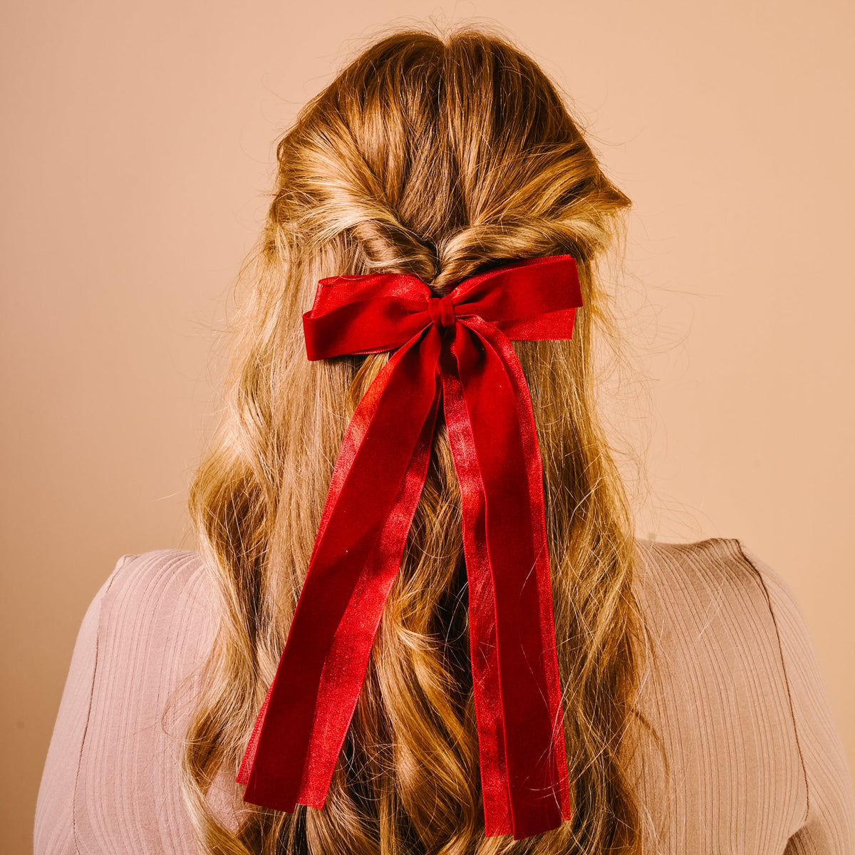 Velvet Luxe Layered Hair Bow, A deep green velvet bow with long tails and a sheer edge, laid flat against a pink background.