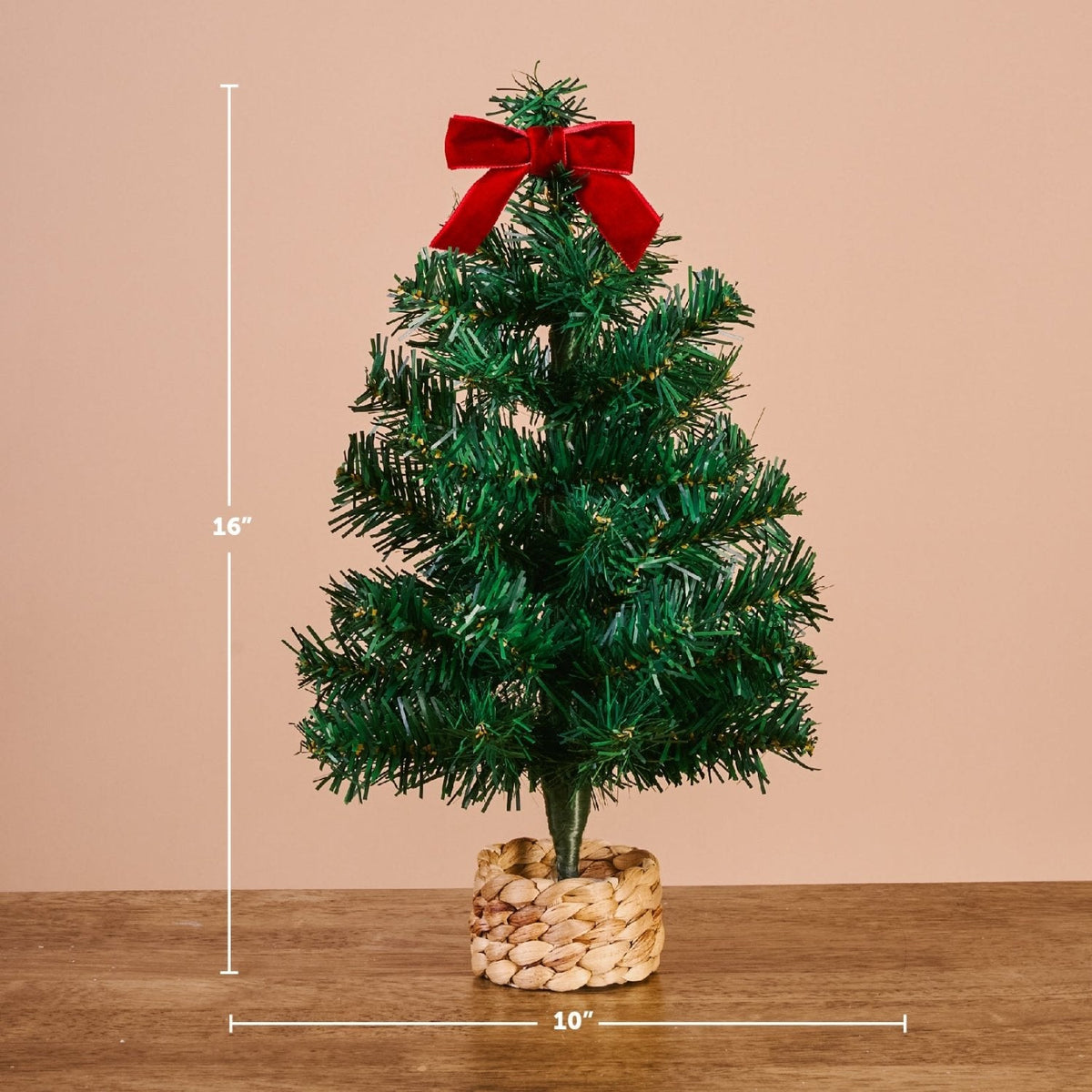 Green Mini Artificial Christmas Tree, A small artificial Christmas tree with full green branches, a red velvet bow at the top, and a woven basket base.