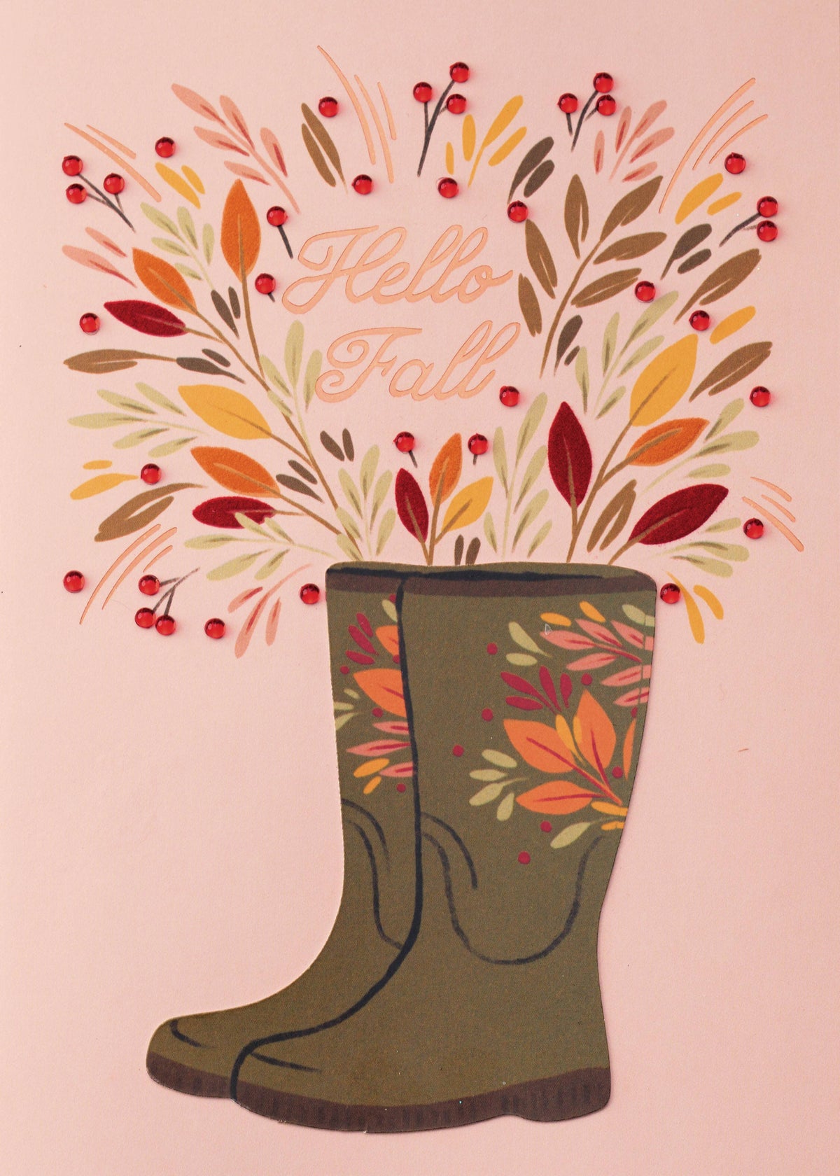 Floral Autumn Boots Greeting Card, A pink card front with a pair of tall olive boots decorated with autumn leaves, holding a bouquet of orange, mustard and burgundy leaves with glossy red berries, and Hello Fall in rose-gold script.