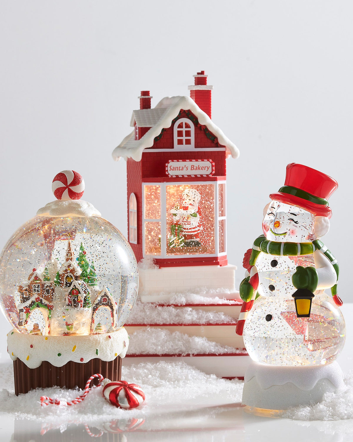 Gingerbread Village Cupcake Lighted Water Globe, A lighted snow globe holding a gingerbread village with evergreens and a church spire, set in a frosted cupcake base with sprinkles and a peppermint candy on top of the dome.