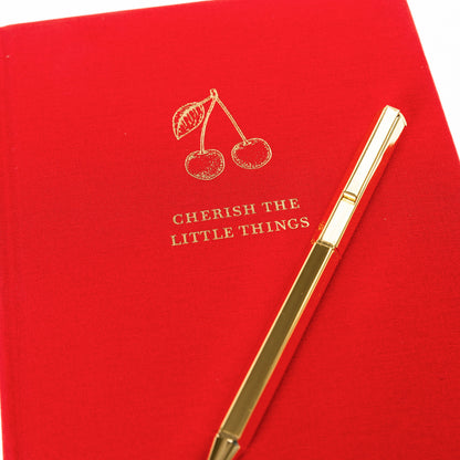 La Petite Presse Cherry Fabric-Bound Journal with Pen, A cherry red fabric journal with gold foil cherries and the words Cherish the Little Things on the cover, paired with a gold twist pen.