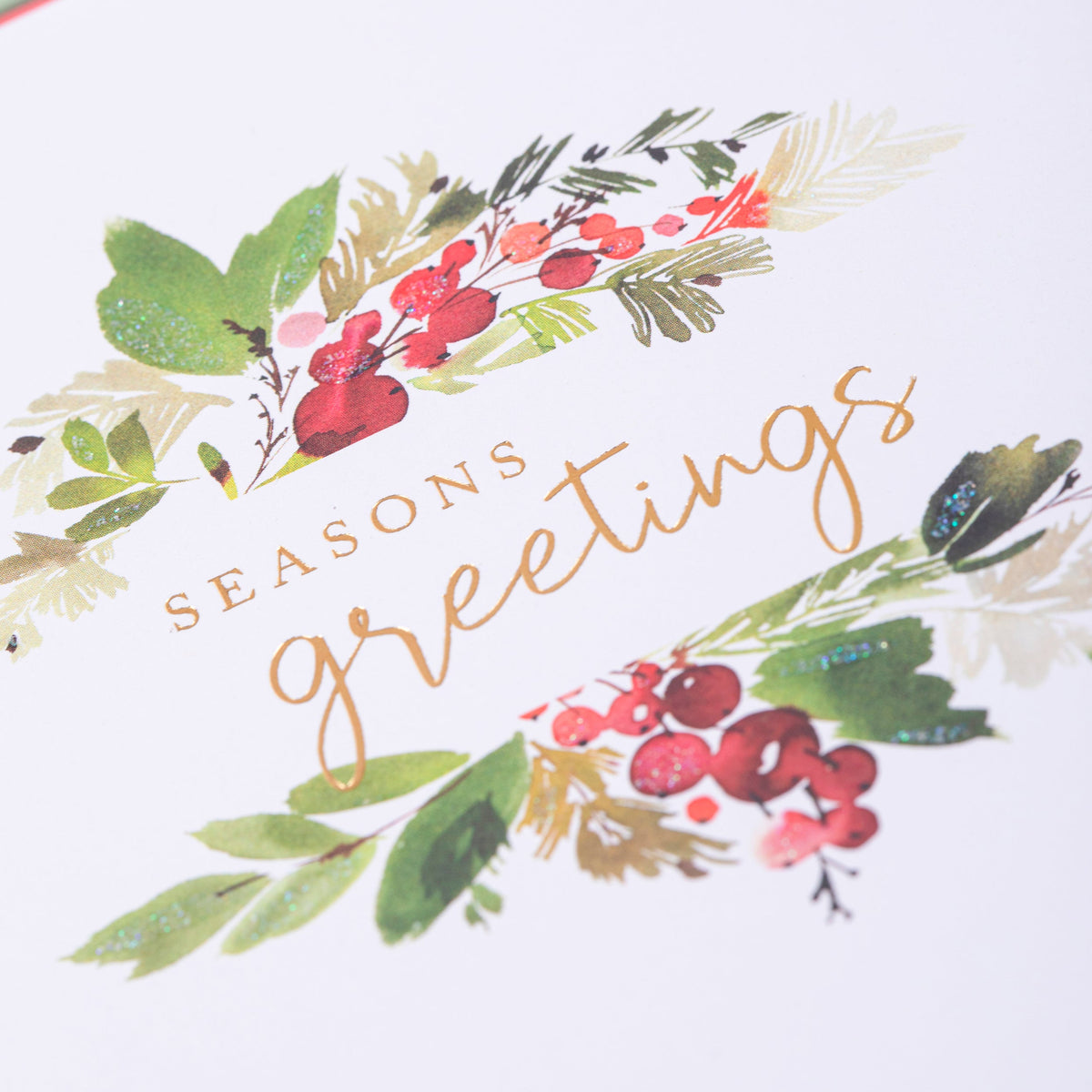 Season's Greetings Holiday Boxed Cards, A Christmas card with a watercolor holly and berry design and gold foil Seasons Greetings script, shown with its red envelope.