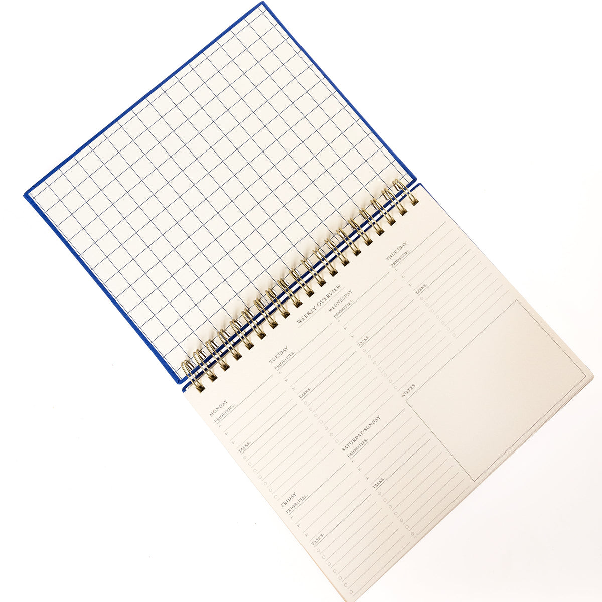 Cobalt Blue Fabric-Bound Weekly Desk Pad, A cobalt blue fabric desk pad reading days weeks in gold foil with a spiral top binding.