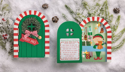 Green Magic Elf Door Set with LED Lights, A green arched wooden elf door with a printed welcome rhyme, standing open in front of a lit printed scene of an elf, presents and a reindeer at a window.