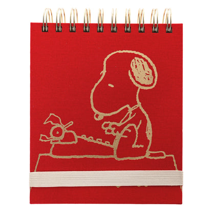 Peanuts Fabric-Bound Notepad, A red fabric-bound notepad with Snoopy typing at his typewriter in gold foil on the cover and gold gilded page edges.