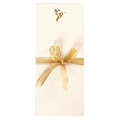 La Petite Presse Hummingbird Gilded Desktop Notepad, A cream notepad with a gold foil hummingbird at the top corner and a gold gilded edge, tied with a gold ribbon.