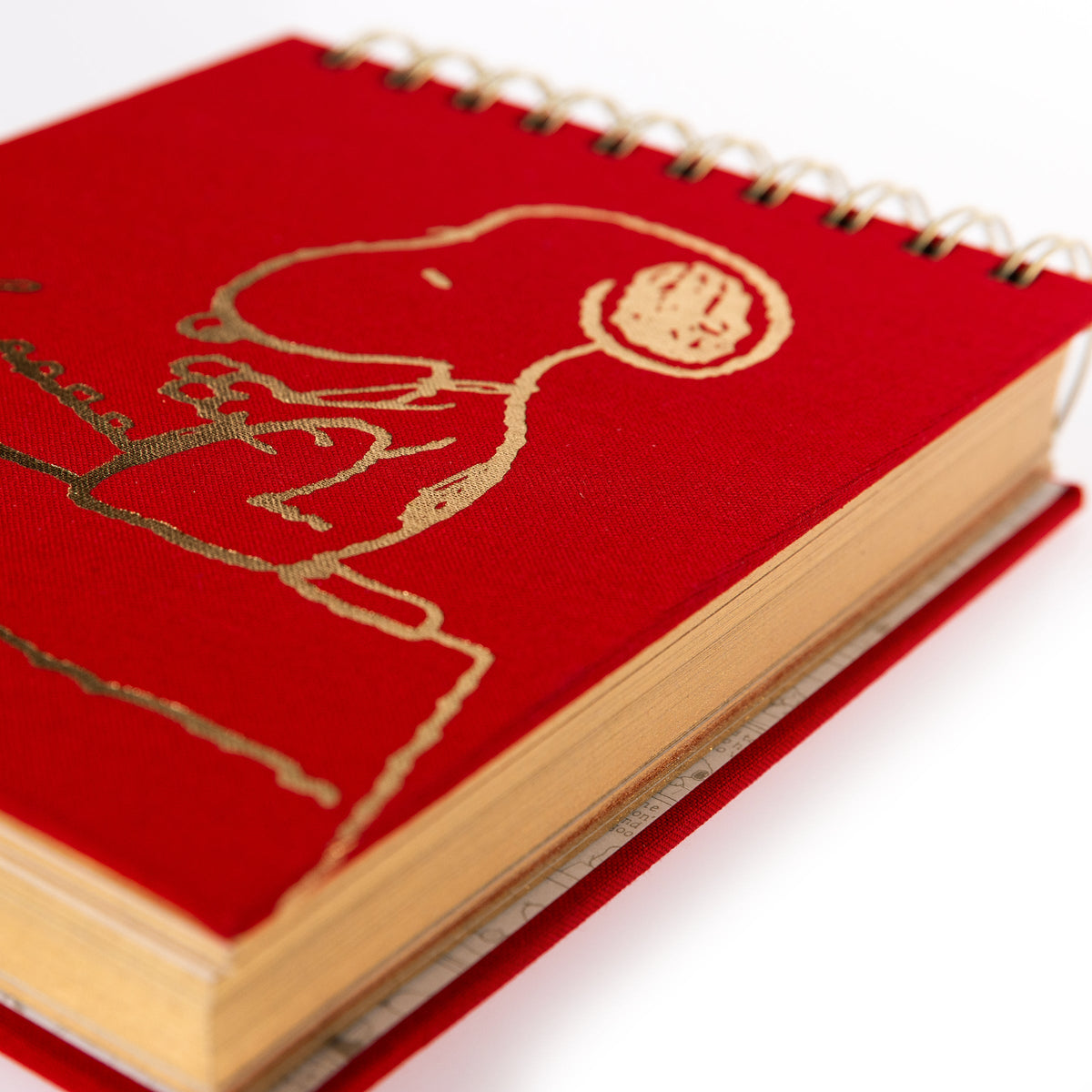 Peanuts Fabric-Bound Notepad, A red fabric-bound notepad with Snoopy typing at his typewriter in gold foil on the cover and gold gilded page edges.