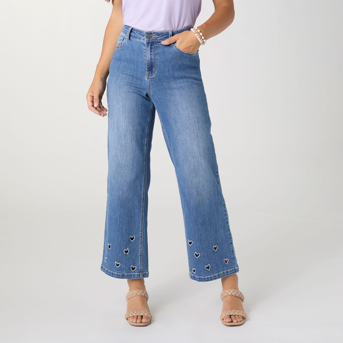 Bambu Soft Heart Cut-Out Wide Leg Ankle Jeans, A woman in medium denim wide leg ankle jeans with heart cut-outs along the hems, a lavender top and braided sandals.
