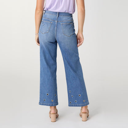 Bambu Soft Heart Cut-Out Wide Leg Ankle Jeans, A woman in medium denim wide leg ankle jeans with heart cut-outs along the hems, a lavender top and braided sandals.