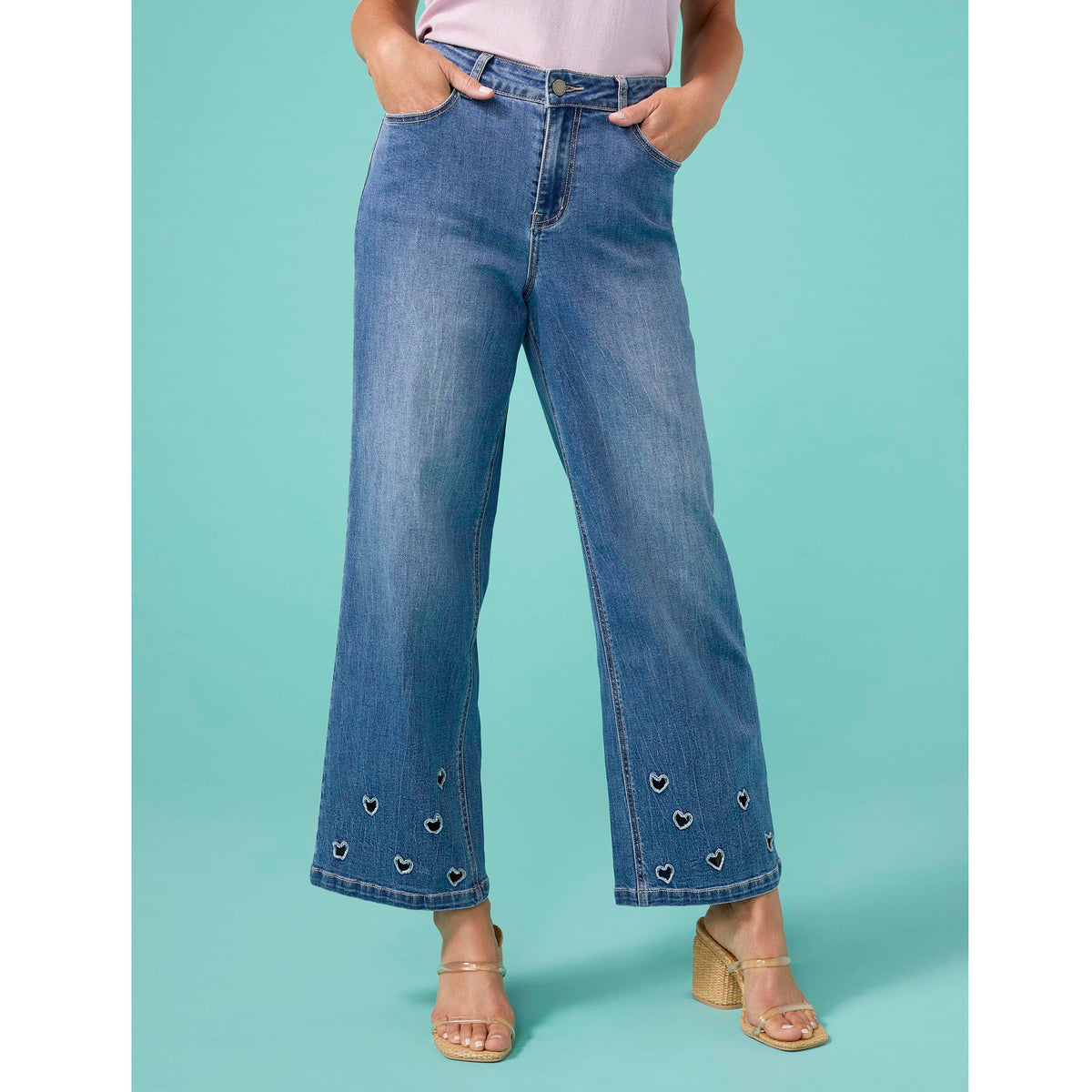 Bambu Soft Heart Cut-Out Wide Leg Ankle Jeans, A woman in medium denim wide leg ankle jeans with heart cut-outs along the hems, a lavender top and braided sandals.