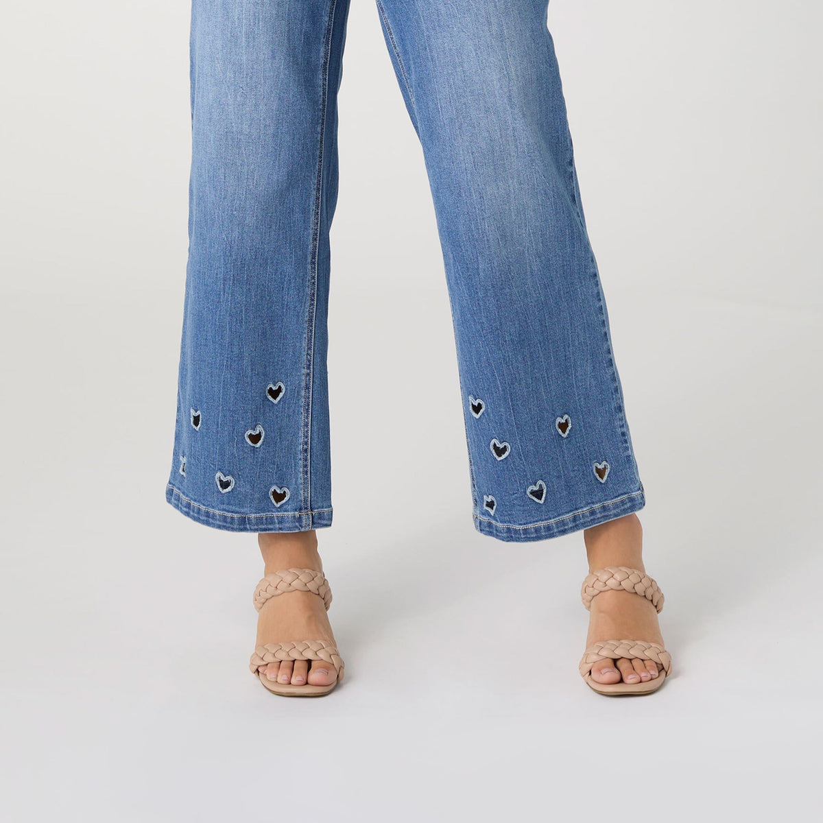 Bambu Soft Heart Cut-Out Wide Leg Ankle Jeans, A woman in medium denim wide leg ankle jeans with heart cut-outs along the hems, a lavender top and braided sandals.