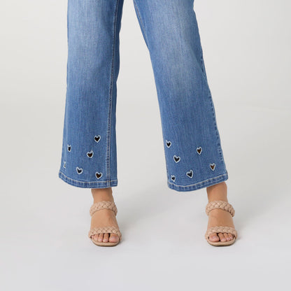 Bambu Soft Heart Cut-Out Wide Leg Ankle Jeans, A woman in medium denim wide leg ankle jeans with heart cut-outs along the hems, a lavender top and braided sandals.