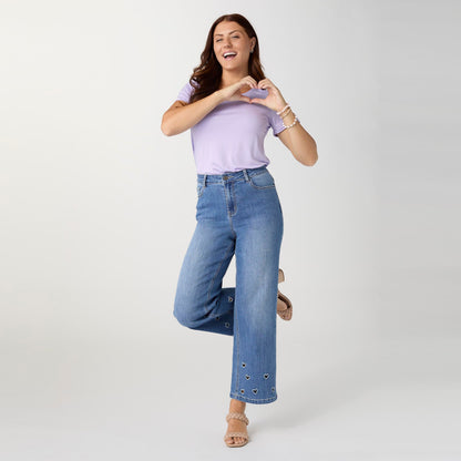 Bambu Soft Heart Cut-Out Wide Leg Ankle Jeans, A woman in medium denim wide leg ankle jeans with heart cut-outs along the hems, a lavender top and braided sandals.