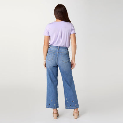 Bambu Soft Heart Cut-Out Wide Leg Ankle Jeans, A woman in medium denim wide leg ankle jeans with heart cut-outs along the hems, a lavender top and braided sandals.