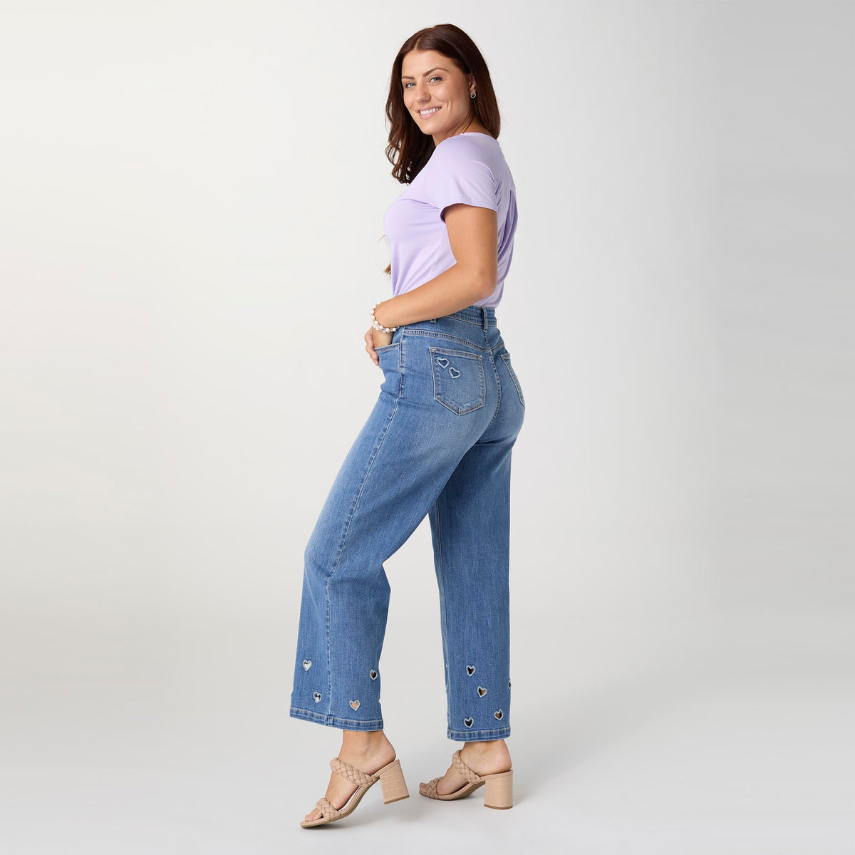 Bambu Soft Heart Cut-Out Wide Leg Ankle Jeans, A woman in medium denim wide leg ankle jeans with heart cut-outs along the hems, a lavender top and braided sandals.