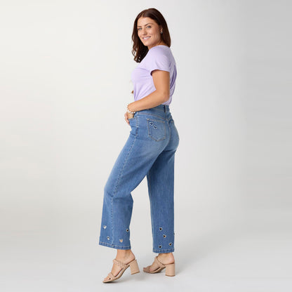 Bambu Soft Heart Cut-Out Wide Leg Ankle Jeans, A woman in medium denim wide leg ankle jeans with heart cut-outs along the hems, a lavender top and braided sandals.