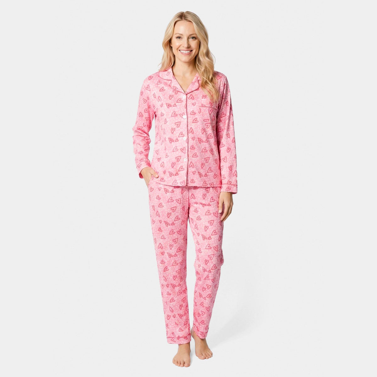 Dreamland Button Front Pajama Top, A smiling woman in a pink heart print button-front pajama top with piping, standing in matching pajama pants.