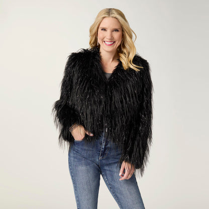 Raven Tinsel Faux Fur Jacket, A smiling woman in a cropped black faux fur jacket with silver tinsel strands over a gray top and blue jeans.