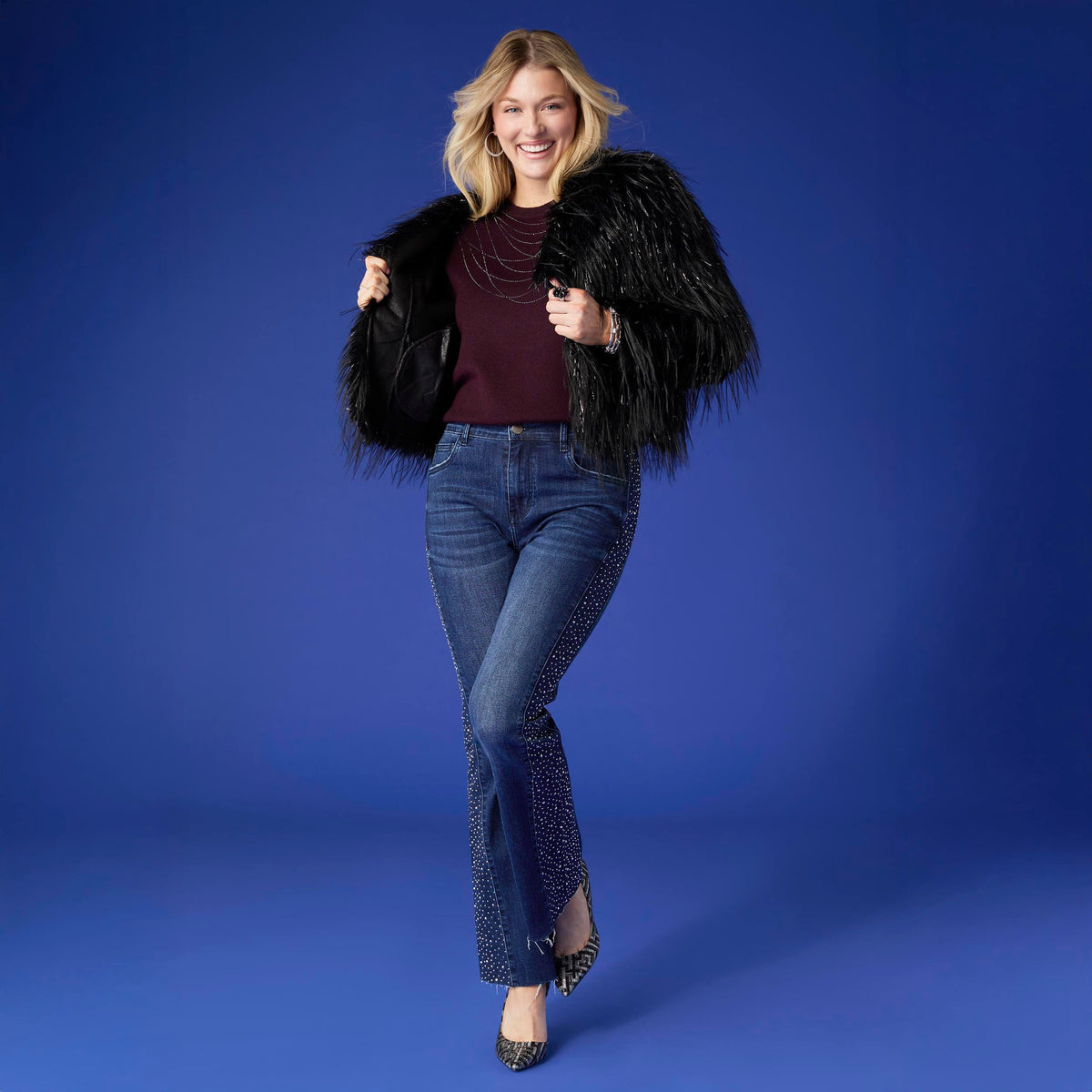 Raven Tinsel Faux Fur Jacket, A smiling woman in a cropped black faux fur jacket with silver tinsel strands over a gray top and blue jeans.