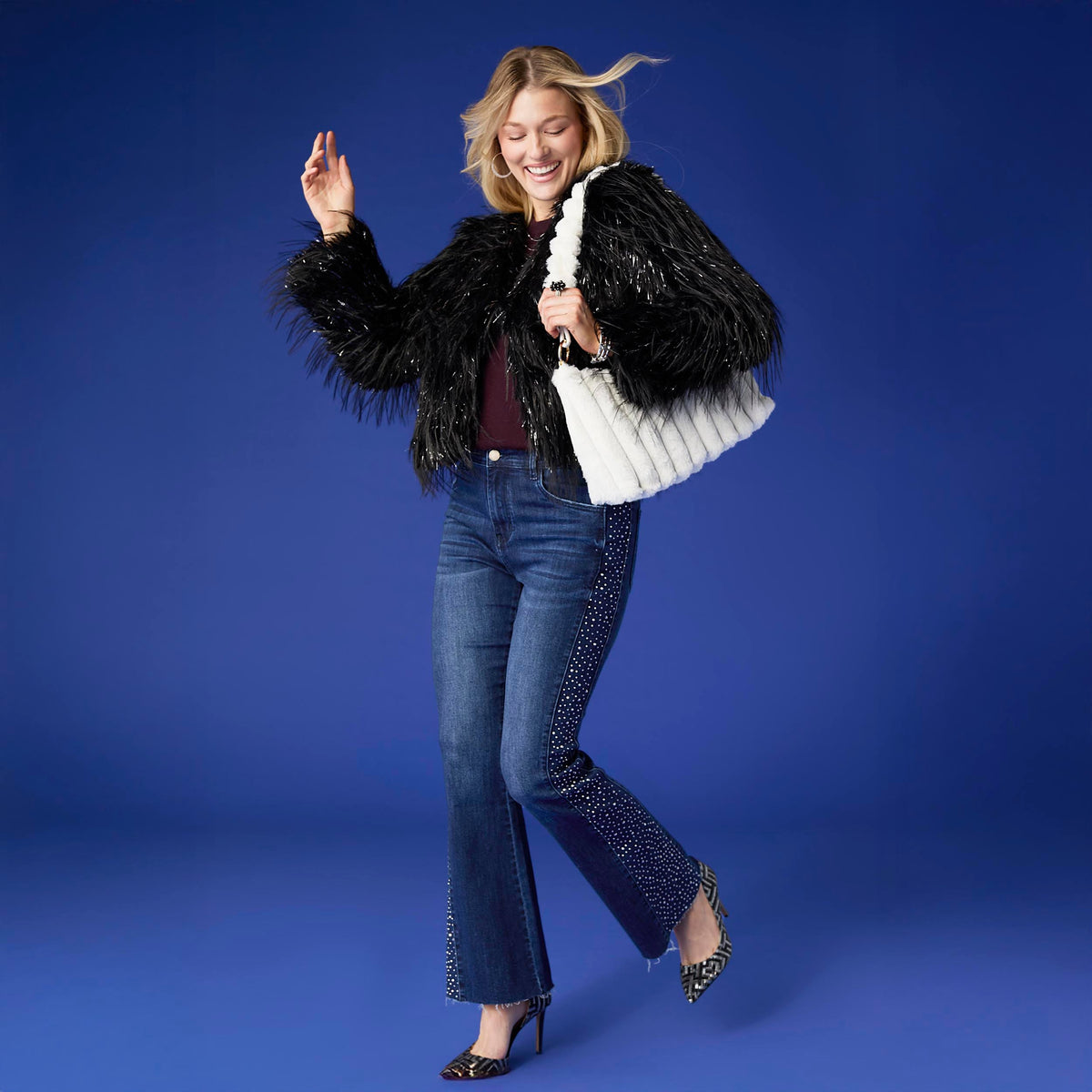 Raven Tinsel Faux Fur Jacket, A smiling woman in a cropped black faux fur jacket with silver tinsel strands over a gray top and blue jeans.