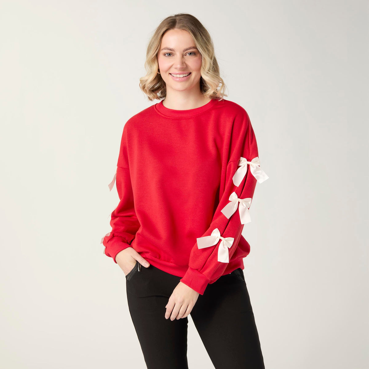 Pleated Bow Sleeve Sweatshirt, A smiling woman in a red crew neck sweatshirt with cream bows down one sleeve and black pants.