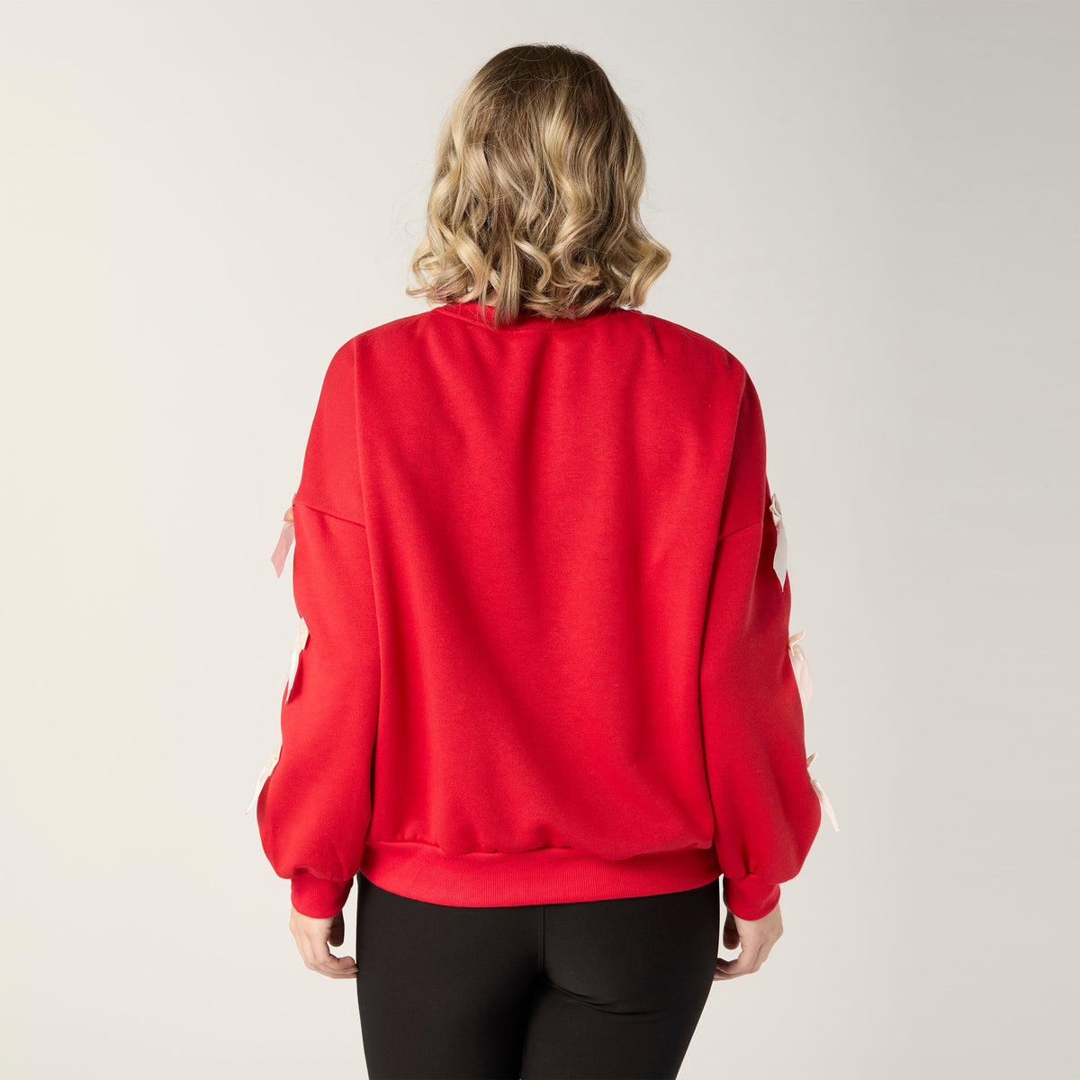 Pleated Bow Sleeve Sweatshirt, A smiling woman in a red crew neck sweatshirt with cream bows down one sleeve and black pants.