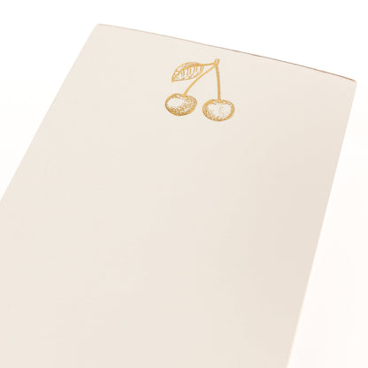 La Petite Presse Cherries Gilded Desktop Notepad, A cream notepad with gold foil cherries at the top and the words Cherish the Little Things stamped in gold at the bottom.