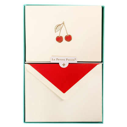 La Petite Presse Cherries Boxed Correspondence Notes, An ivory notecard with gold foil cherries filled in red glitter, paired with a cream envelope lined in bright red.