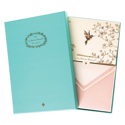 La Petite Presse Hummingbird Boxed Correspondence Notes, A cream notecard with a colorful hummingbird and gold magnolia branch line art, paired with a blush pink lined envelope.
