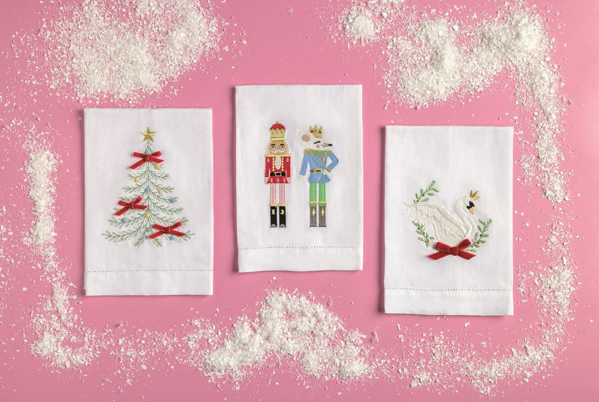 Crowned Swan Embroidered Hand Towel, A folded white hand towel embroidered with a white swan wearing a gold crown, framed by green sprigs, with a red velvet bow and a hemstitched bottom border.