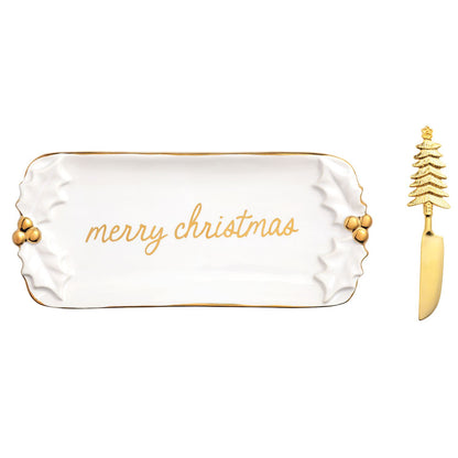 Gold Holly Butter Dish and Spreader Set, A white stoneware butter dish with sculpted holly leaves at each end, gold berries, a gold rim and merry christmas in gold script, shown with a gold spreader with a Christmas tree handle.