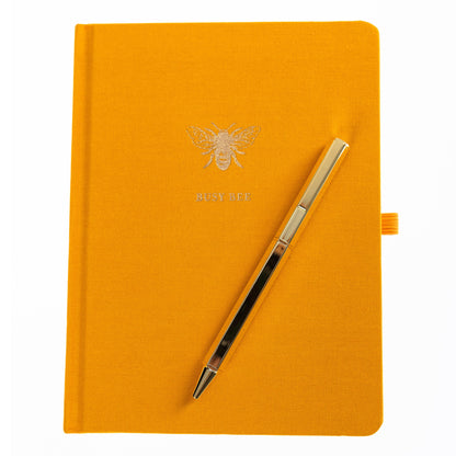 La Petite Presse Bee Fabric-Bound Journal with Pen, A marigold fabric journal with a gold foil bee and the words Busy Bee on the cover, paired with a gold twist pen.