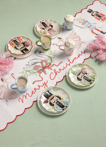 Nutcracker Merry Christmas Table Runner, Long white table runner with a red scalloped edge, painted with nutcracker soldiers, crowned mice holding swords, pink ballerinas and a swan in a wreath, and Merry Christmas in red script.