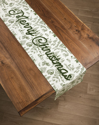 Green Toile Merry Christmas Table Runner, A long cream cotton table runner printed in green Christmas toile with Merry Christmas embroidered in green script across the center.