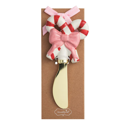 Candy Cane Cheese Spreader with Hand-Painted Handle, A gold toned spreader with a hand-painted candy cane handle striped in red and white and a pink bow, mounted on a kraft card.