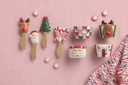 Reindeer Handle Cheese Spreader, 5.5 Inch, A brass-toned spreader with a hand-painted reindeer head handle, dark antlers and a red nose, mounted on a kraft card with a red ribbon bow.