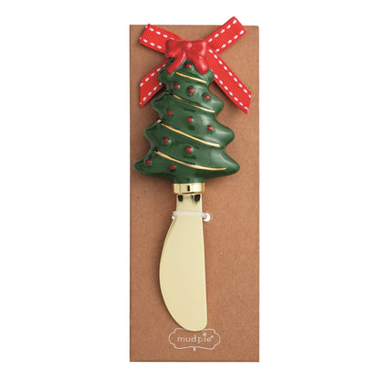 Christmas Tree Figural Cheese Spreader, A gold-toned spreader with a hand-painted green Christmas tree handle trimmed in red baubles, gold garland lines and a red bow, mounted on a kraft card with a red ribbon.