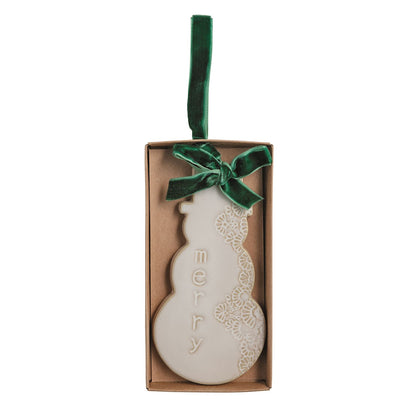 White Snowman Ceramic Ornament with Velvet Bow, A flat white ceramic ornament shaped like a snowman with pressed lace texture down one side, the raised word merry down the other, and a green velvet bow, shown in a kraft gift box.