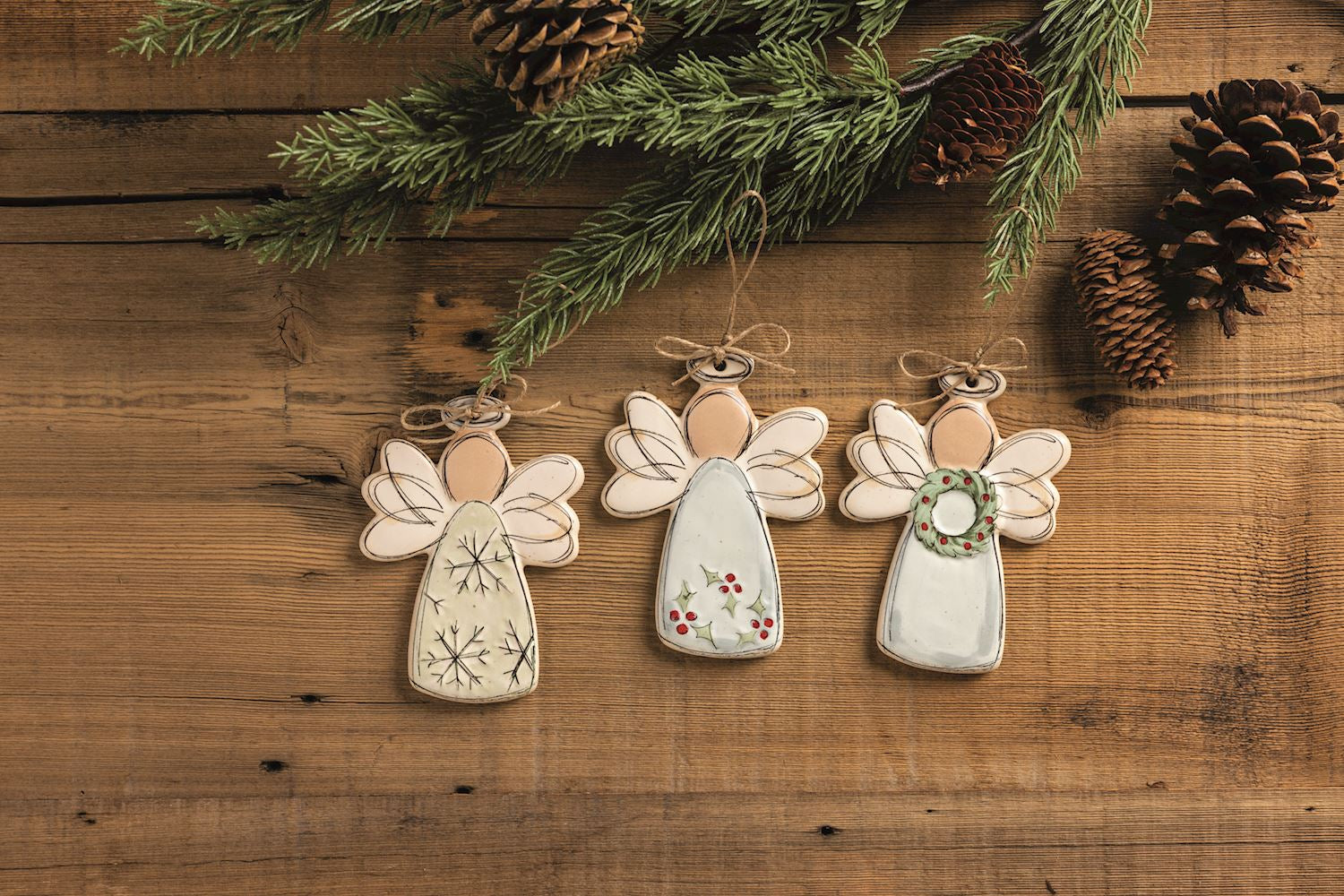 Snowflake Angel Stoneware Ornament, 5.25 Inch, A flat speckled cream stoneware angel ornament with sketched black line wings, a halo and snowflakes on the gown, hanging from a twine loop tied in a small bow.