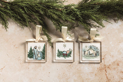 Nativity Scene Acrylic Ornament, Square clear acrylic ornament printed with the Christ child asleep in a bed of pine and holly tied with a red bow, a star above, hung from a cream grosgrain ribbon bow.