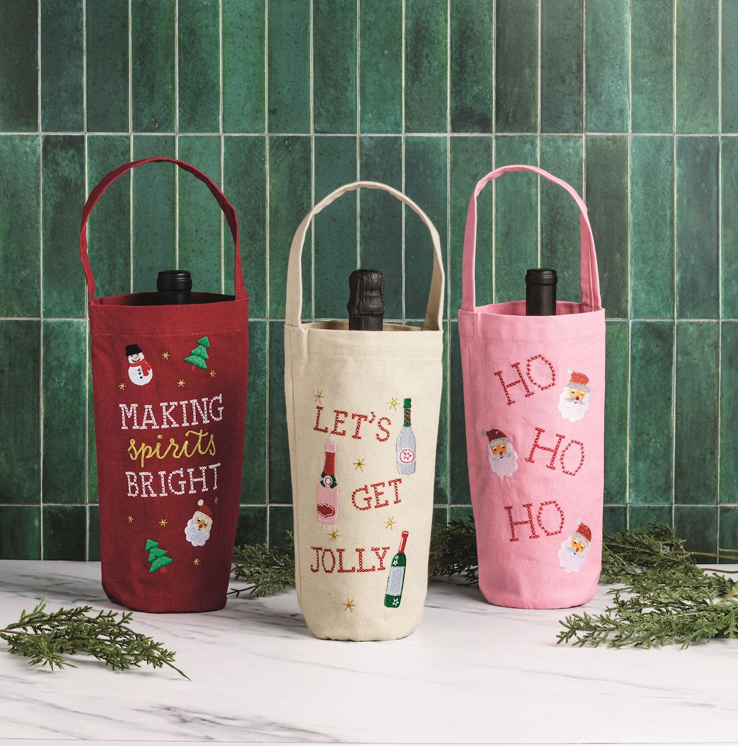 Making Spirits Bright Embroidered Wine Bag, A red canvas wine bag with a long handle, embroidered MAKING spirits BRIGHT in white and gold with a snowman, a Santa face, green trees and gold stars, holding a wine bottle.