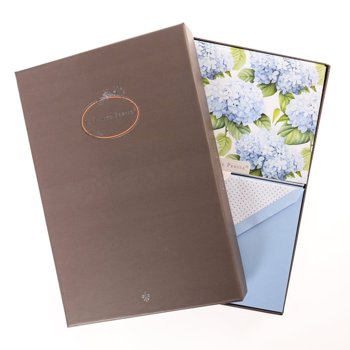 La Petite Presse Hortensia Boxed Correspondence Notes, A brown gift box open to a white notecard printed with powder blue hydrangea blooms, paired with a matching blue envelope.
