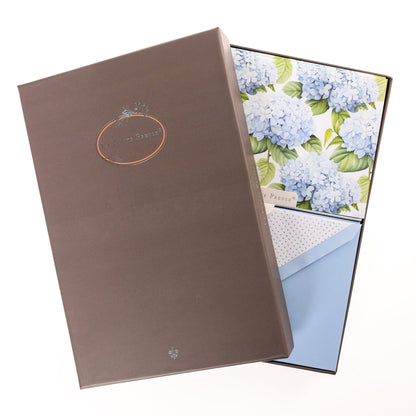 La Petite Presse Hortensia Boxed Correspondence Notes, A brown gift box open to a white notecard printed with powder blue hydrangea blooms, paired with a matching blue envelope.