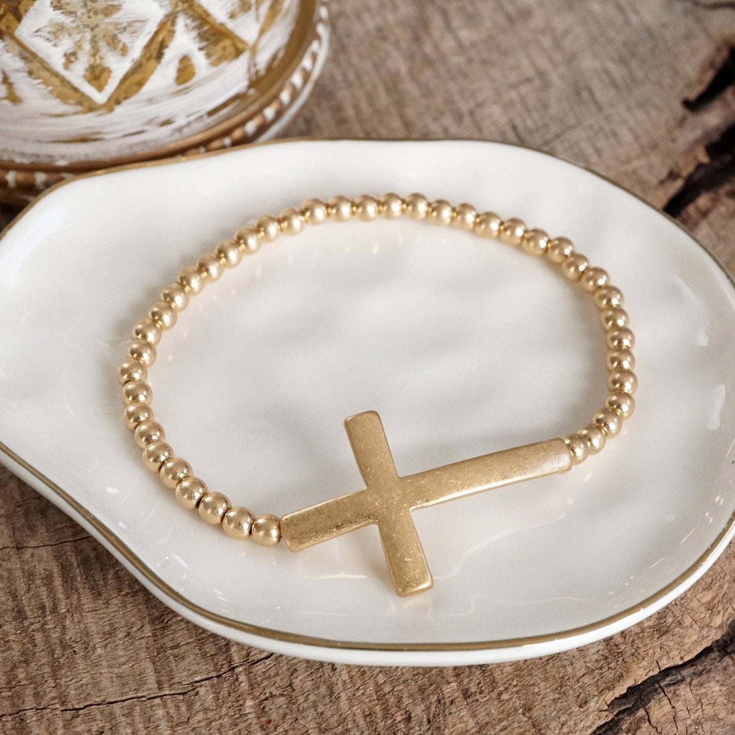 Pulsera elástica minimalista con cruz en tono dorado desgastado y cuentas de bola
