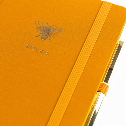 La Petite Presse Bee Fabric-Bound Journal with Pen, A marigold fabric journal with a gold foil bee and the words Busy Bee on the cover, paired with a gold twist pen.