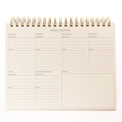 Cobalt Blue Fabric-Bound Weekly Desk Pad, A cobalt blue fabric desk pad reading days weeks in gold foil with a spiral top binding.
